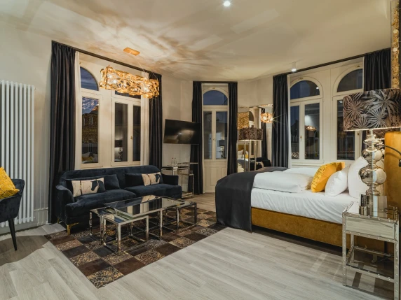 Superior Rooms hotel room at BS Boutique Hotel Heidelberg. Equipped with a golden bed, dark blue sofa, dark curtains, and golden lamp.